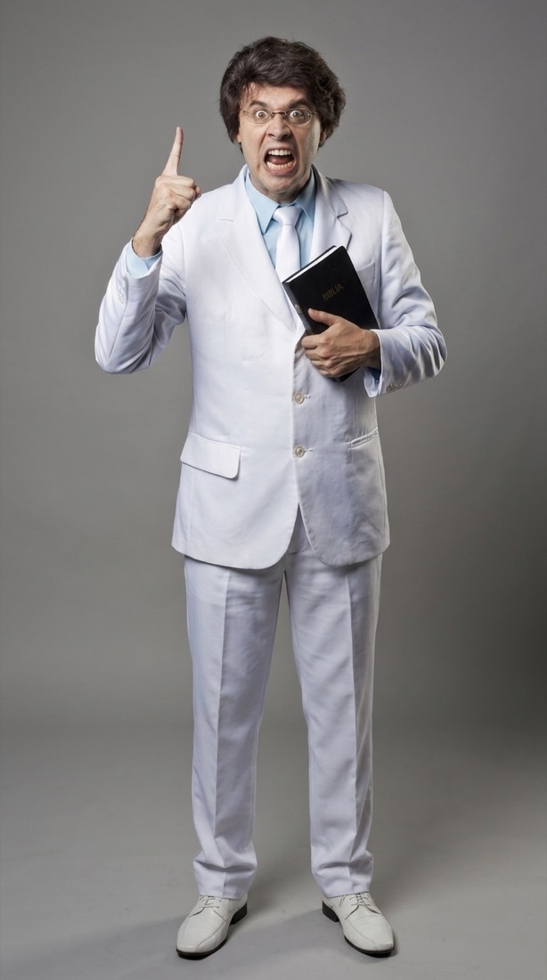 Jeringa caracterizado como el Hermano James, con traje blanco y una Biblia, señalando hacia arriba